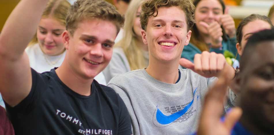 two young men smile in a crowd of other students